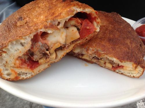 A cross-section of a stuffed calzone filled with meat, cheese, and pepperoni, served on a white plate.