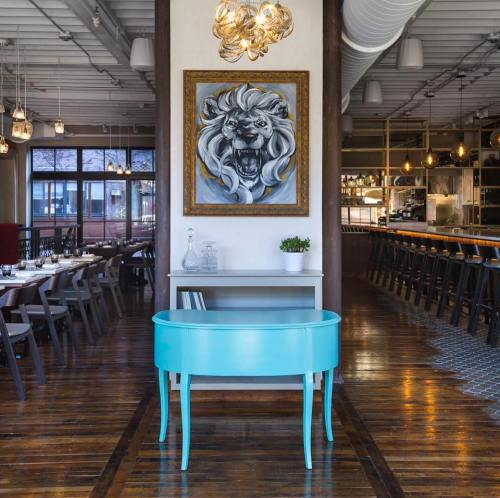 A modern restaurant interior featuring a turquoise table, wooden floors, and a lion painting on the wall.