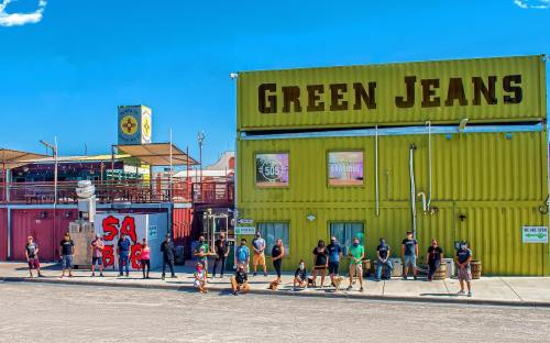 A group of people stands outside a bright green building labeled "Green Jeans" on a sunny day.
