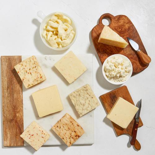 A variety of cheeses displayed on a marble and wooden board, with cheese curds and a knife on the side.