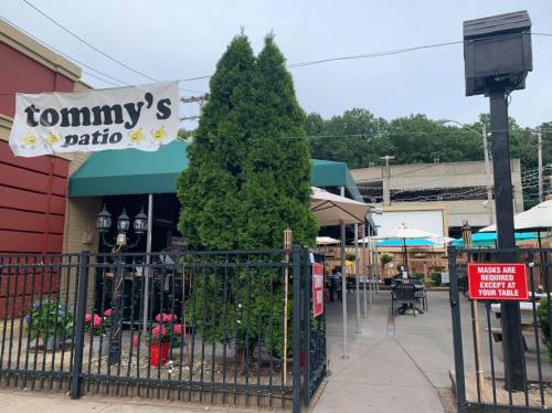 Outdoor dining area at Tommy's Patio, featuring umbrellas, greenery, and a sign about mask requirements.