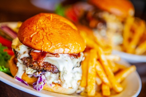 A close-up of a juicy burger with bacon, lettuce, and sauce, served with crispy fries on the side.