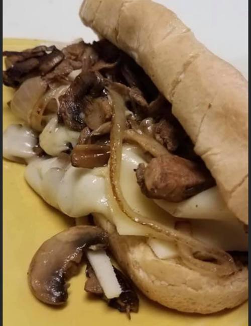A sandwich filled with grilled chicken, mushrooms, onions, and melted cheese on a toasted hoagie roll.