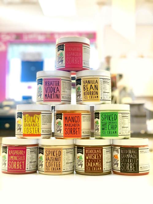 A colorful display of various ice cream and sorbet tubs stacked in a pyramid, featuring unique flavors.