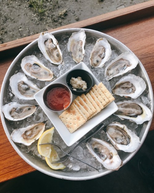 A platter of fresh oysters on ice, served with lemon, crackers, cocktail sauce, and horseradish.