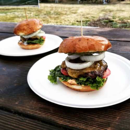 Two delicious burgers on white plates, topped with lettuce, tomato, onions, and served on toasted buns.