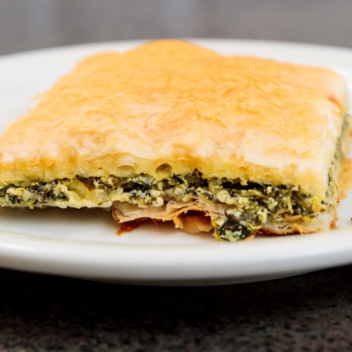 A slice of flaky pastry filled with spinach and cheese, served on a white plate.
