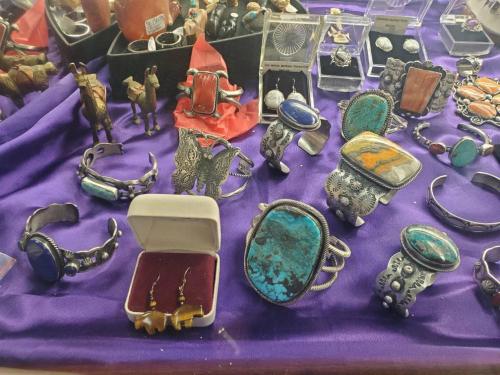 A display of various silver and turquoise jewelry pieces, including rings, bracelets, and earrings on a purple cloth.