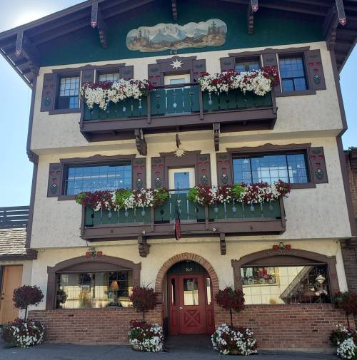 Charming building with green balconies, flower boxes, and decorative details, set against a clear blue sky.