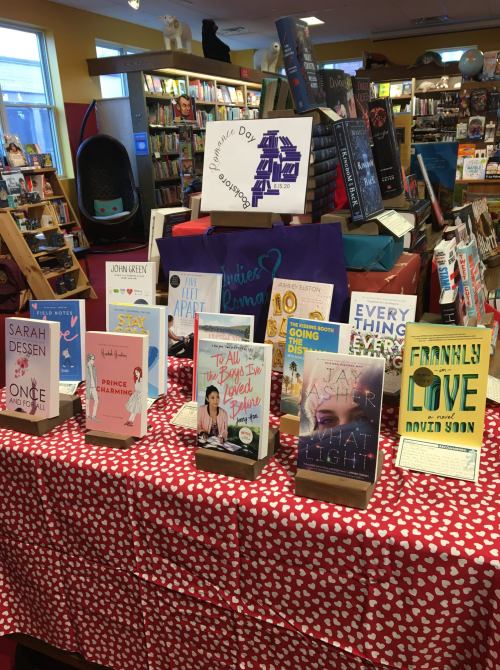 A display of books on a table in a bookstore, featuring various titles and a colorful backdrop.