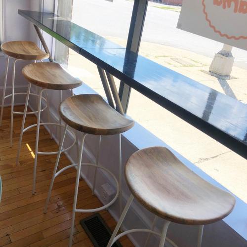 A row of wooden bar stools at a sleek counter by a large window, with sunlight streaming in.