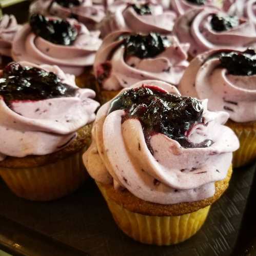 Close-up of cupcakes with purple frosting and a dollop of dark berry jam on top, arranged on a tray.