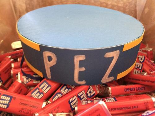 A blue and yellow PEZ dispenser lid sits atop a pile of red PEZ candy rolls.