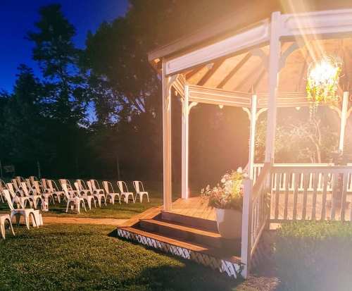 A gazebo illuminated at night, surrounded by empty white chairs arranged on a grassy area.