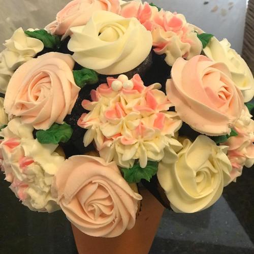 A decorative cake bouquet featuring pink and white frosting roses and flowers arranged in a cone shape.