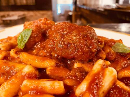 A close-up of pasta with meatballs in marinara sauce, garnished with fresh basil leaves.