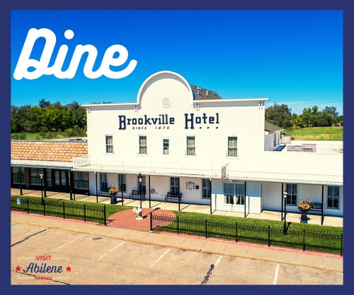 Aerial view of the Brookville Hotel, featuring a blue sky and inviting outdoor dining area. Text overlay: "Dine."