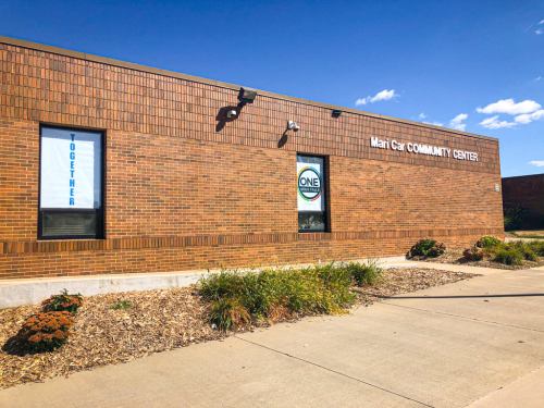Exterior of Mari Car Community Center with windows displaying "TOGETHER" and "ONE" signs, surrounded by landscaping.