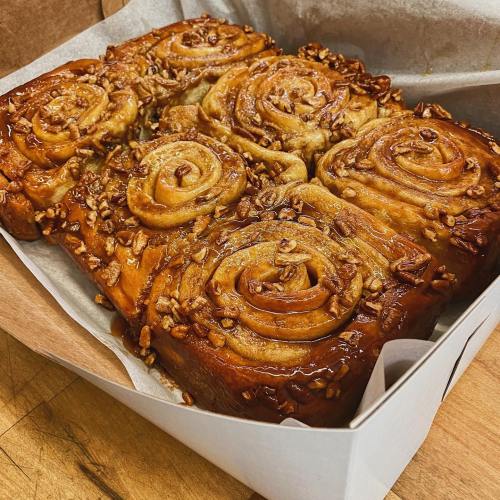 A box of freshly baked cinnamon rolls topped with nuts and caramel, arranged in a spiral pattern.