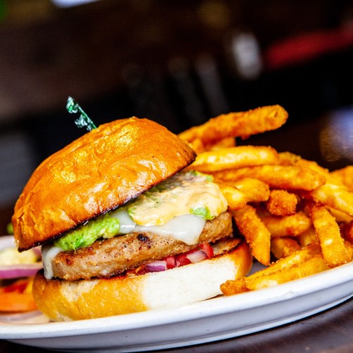 A juicy burger with avocado and cheese, served with crispy fries on a white plate.