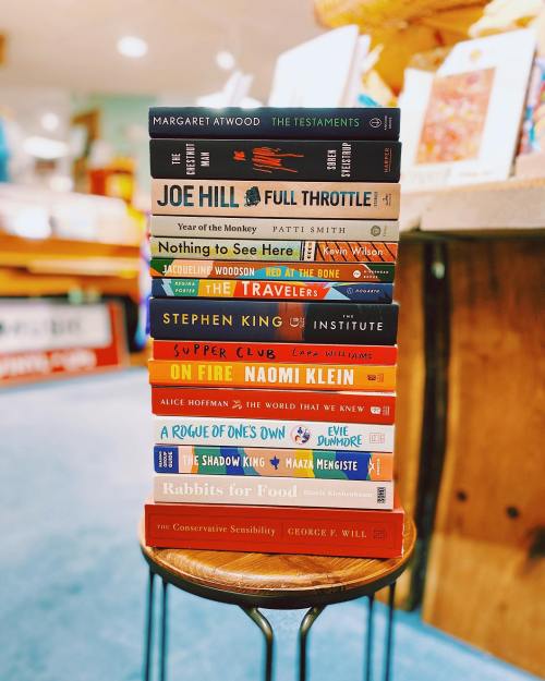 A stack of books by various authors, including Margaret Atwood and Stephen King, displayed on a small table.