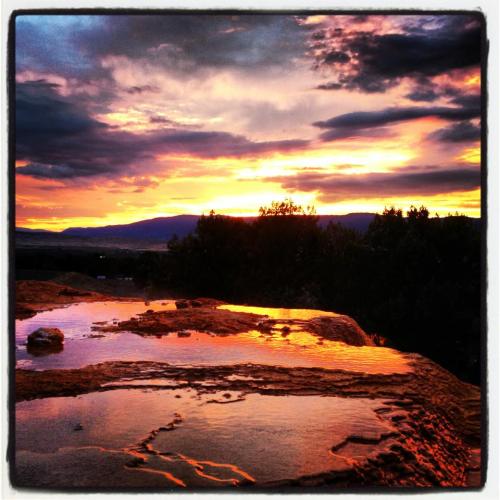 Sunset over a rocky landscape, with vibrant orange and purple hues reflecting in puddles on the ground.