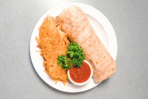A plate with a burrito, hash browns, a small bowl of salsa, and a sprig of parsley on a gray table.