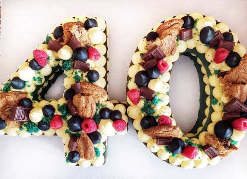 A large cake shaped like the numbers "40," decorated with frosting, cookies, chocolate, and berries.