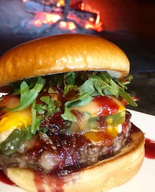 A juicy burger with melted cheese, fresh greens, and a tangy sauce, served on a toasted bun with a warm fire in the background.