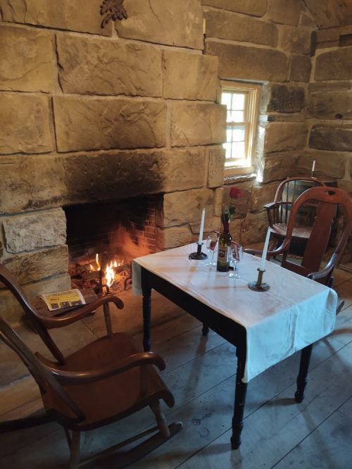 Cozy dining setup in a rustic stone room, featuring a table with candles, a rose, and a fireplace.