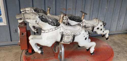 Three vintage carousel horses on a red platform, with a rustic wooden backdrop.
