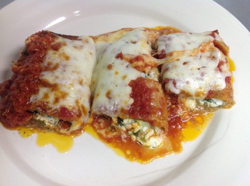 Three cheesy, baked cannelloni filled with spinach and ricotta, topped with marinara sauce on a white plate.