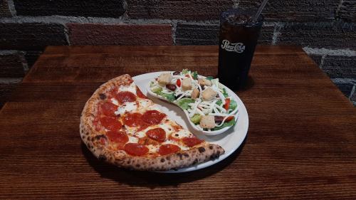 A plate with a slice of pepperoni pizza, a side salad with croutons, and a glass of soda on a wooden table.
