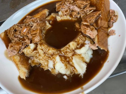 A plate of toast topped with shredded meat and gravy, served with a side of mashed potatoes and more gravy.