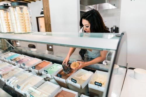 A woman scoops ice cream into a cone at a colorful ice cream shop display.