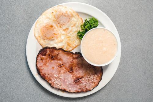A plate with two fried eggs, a slice of ham, and a bowl of grits, garnished with a parsley sprig.