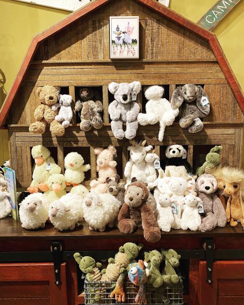 A display of various plush animals, including bears, koalas, sheep, and ducks, arranged on a wooden shelf.