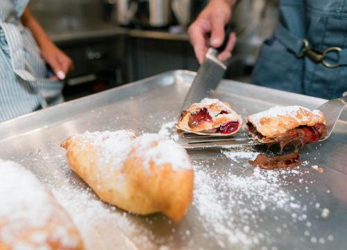 A close-up of pastries filled with jam and chocolate, dusted with powdered sugar on a baking tray.