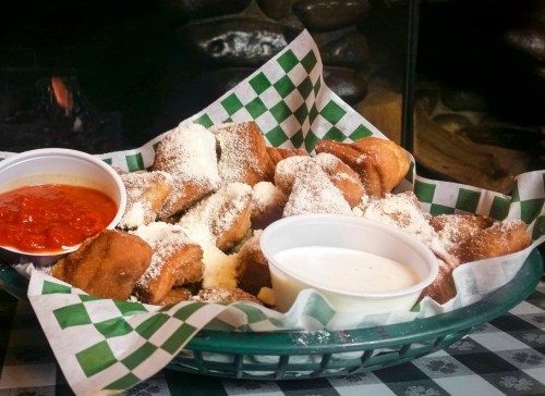 A basket of fried dough bites dusted with powdered sugar, served with marinara and ranch dipping sauces.