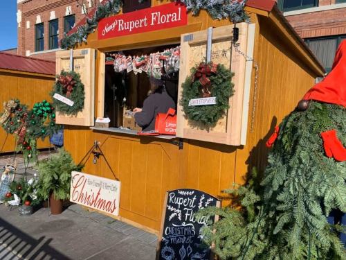 A festive wooden stall decorated for Christmas, featuring wreaths, garlands, and a sign for Rupert Floral's Christmas market.