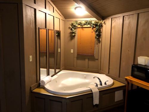 A cozy bathroom featuring a corner jacuzzi, wooden walls, a mirror, and a small table with a microwave.