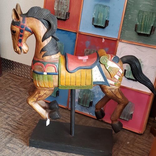 A colorful wooden carousel horse sculpture, featuring intricate details and a vibrant saddle, displayed on a stand.