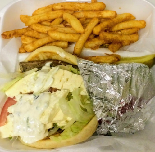 A container with a pita sandwich filled with lettuce, tomato, and feta cheese, alongside a serving of French fries.