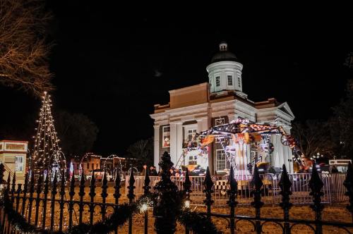 A festive scene at night featuring a decorated building, a carousel, and a lit Christmas tree.