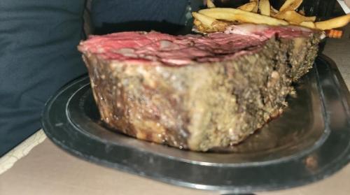 A close-up of a large, juicy roast beef slice on a metal platter, accompanied by golden fries.