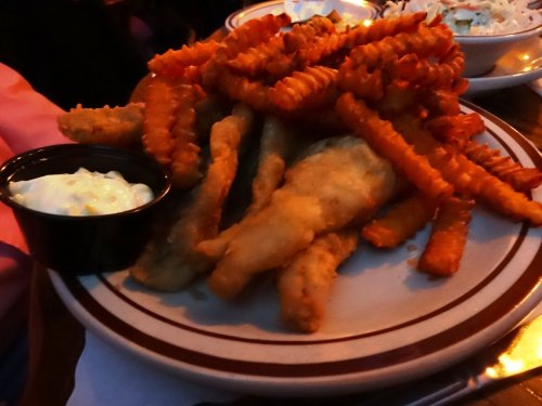 A plate of golden crinkle-cut fries and crispy fish sticks, served with a small cup of dipping sauce.
