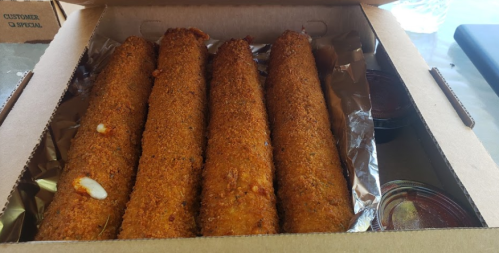 Four golden-brown, crispy fried items in a takeout box, accompanied by two small containers of sauce.