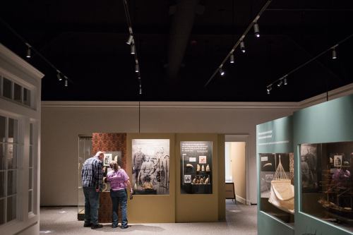 Two visitors explore an exhibit in a dimly lit museum, examining displays and artifacts on the walls.