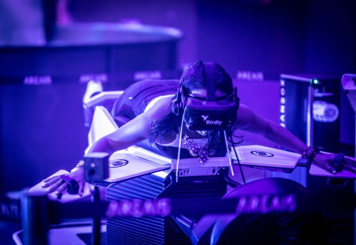 A person wearing a VR headset lies on a futuristic device, immersed in a virtual experience with purple lighting.