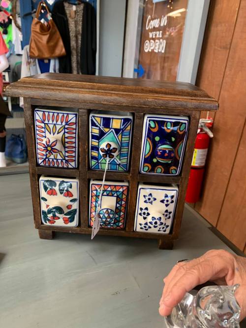 A small wooden cabinet with colorful, patterned tiles on the front, displayed on a table in a shop.